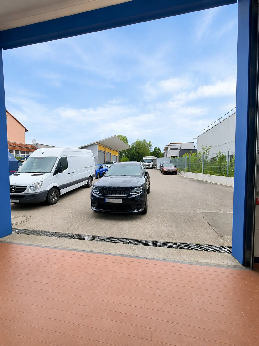 Blick aus dem ENZ Werkstatttor auf den Vorplatz mit Fahrzeugen